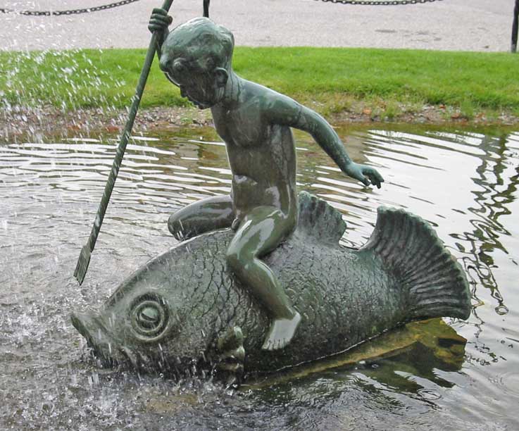 Bronseskulptur av en gutt som svinger en harpun mens han rir på ryggen av en stor fisk ved Jernbanestasjonen i kristiansand